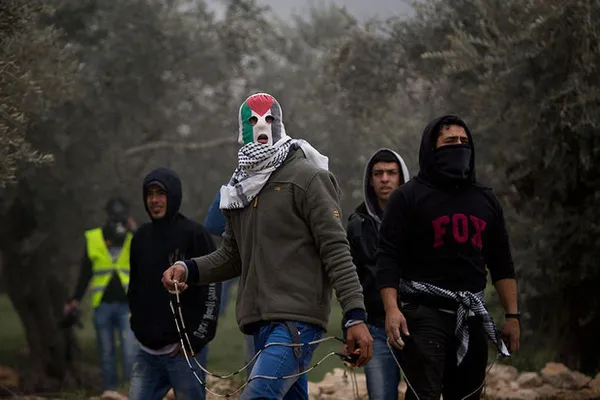 مرد فلسطینی که از پرچم این کشور به عنوان نقاب استفاده کرده، با قلاب سنگ به سمت سربازان رژیم صهیونیستی حمله می&zwnj;کند.

