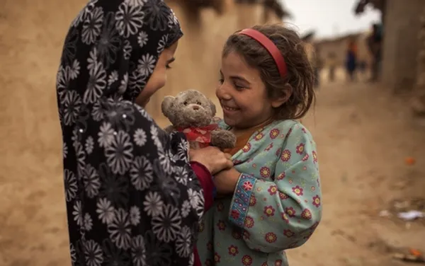 کودک پناهجوی افغان لبخندزنان با اهدای خرس عروسکی به همراه روبانی به شکل قلب، روز ولنتاین را به دوستش تبریک می&zwnj;گوید. /رویترز
