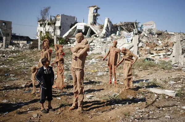 کودک فلسطینی در حال نگاه کردن به مجسمه هایی است که توسط ایاد صباح، هنرمند فلسطینی، در خرابه های بجا مانده از جنگ اخیر غزه ساخته شده است. این مجسمه ها نماد آوارگان فلسطینی است که در حال گریز از خانه هایشان هستند./Reuters-Euronews
